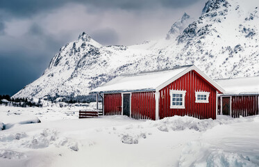 Stunning winter landscape. Winter scenery, Lofoten Islands, Norway. Traditional fishing hut in front of the snowy mount under sunlight. Popular travel destination of world.