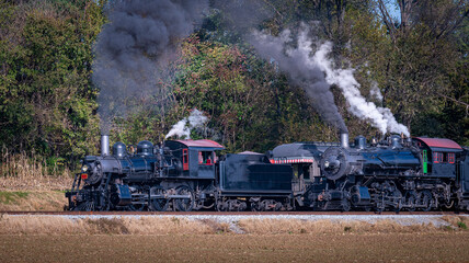 Fototapeta na wymiar A View of Two Steam Engines, blowing Smoke and Steam One Pulling Ahead of the Other on a Sunny Day