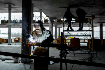 Construction of a production facility. Two handymen perform welding and grinding at their workplace in the workshop. Man in protective helmet and gear