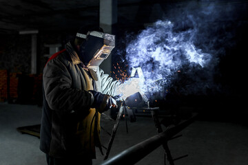 Construction of a production facility. The master performs welding and grinding at his workplace in the workshop. Man in protective helmet and gear