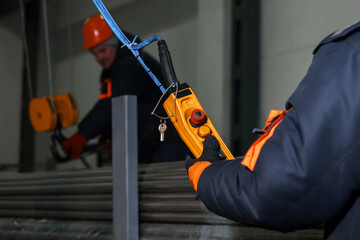 Close-up of a worker using a remote control overhead crane in a factory warehouse to load stainless...