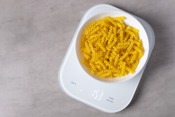 Raw fusilli pasta in a white plate on the electronic kitchen scales