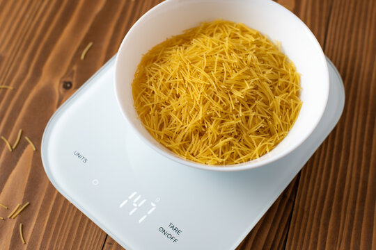 Raw filini vermicelles pasta in a white plate on the electronic kitchen scales