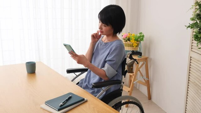 家でスマホを使う車椅子に乗った障がい者女性
