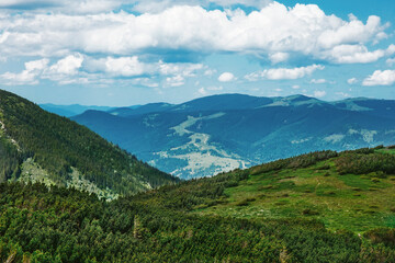 Fototapeta na wymiar Beautiful scenery of forested Carpathian mountains in summer, green in foreground, blue in background, the road runs away; amazing nature landscape with expressive voluminous sky and clouds