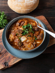Beef stew with cabbage and vegetables. Served on rustic and wooden background with homemade ciabatta bread. Top view