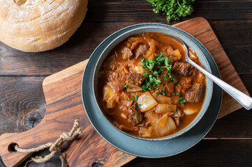 Brown beef stew with cabbage and vegetables. Served with homemade ciabatta bread on wooden table