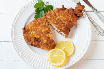 Breaded chicken schnitzel with lemon and parsley isolated on a white plate on white background. 