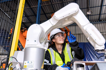 Fototapeta premium Young female asian service engineer holding robot controller operate robot arm automation factory