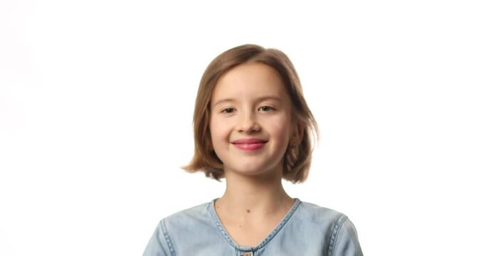 Pretty little girl in casual denim dress blowing, inflate yellow balloon on white background, studio