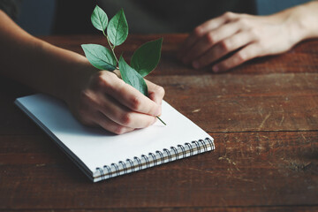 Young woman taking notes, writing with green plant as pen on notebook, eco lifestyle concept, list...