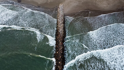 Aerial Top View Drone Footage Of Ocean Waves Reaching Shore stone breakwater - 566611889