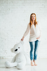 red-haired pregnant girl in a light blouse and blue jeans with a teddy bear