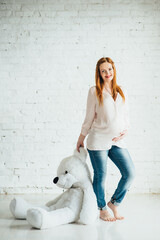 red-haired pregnant girl in a light blouse and blue jeans with a teddy bear