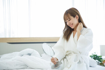 Woman sitting on the bed with the mirror after waking up, side view, entering a day happy and relaxed after good night sleep. Sweet dreams, good morning, new day, weekend, holidays concept.
