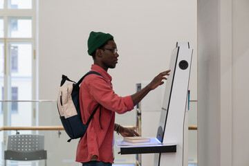 Student African man using self-service electronic terminal to pay for goods in store without...