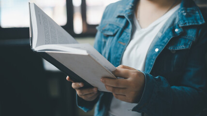 Closeup on female with book in the library in sunny day.Beautiful woman holding a book in hands while reading it on a bookshelf background, in a library.