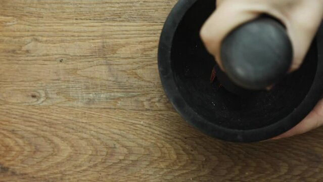 Female hand grinding spices in stone mortar. close up top view, red hot pepper mexican spices, cooking healthy concept wooden background