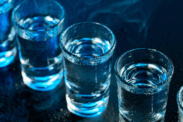 Wet glasses of vodka in smoke on dark blue background.