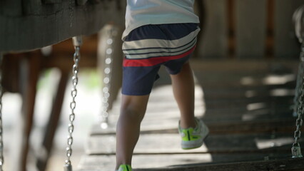 One active child running on playground structure. Kid having fun at wood bridge outdoors