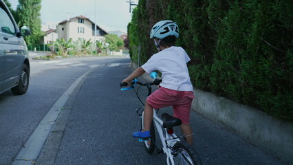 Obraz premium Little boy riding bicycle in city sidewalk. Child rides bike with wheels in street wearing helmet