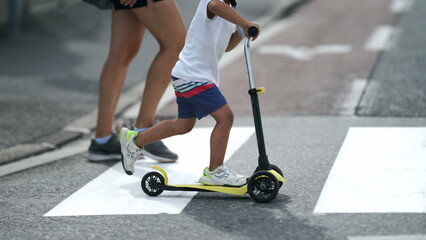 Child crossing street with scooter on zebra lines. Parent and kid on crosswalk in sunny day. Active small boy rides trandportation crosses sidewalk © Marco