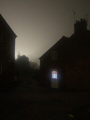 Window glowing in the door of a spooky house in the fog at night
