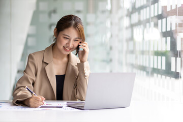 Attractive Asian businesswoman in office using smartphone and talking with business partner on mobile phone.