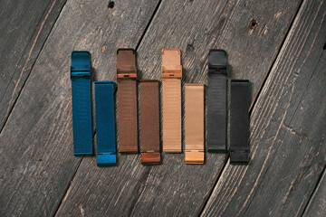 Colourful steel watch straps laying on the dark brown rustic wooden table.