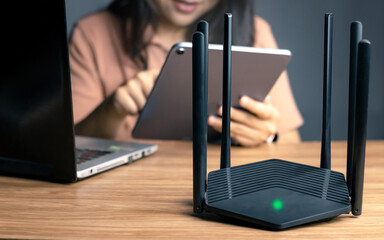 Selective focus at router. Internet router on working table with blurred happy woman using tablet...