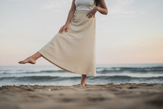 Anonymous carefree young Hispanic lady kicking sand on seashore