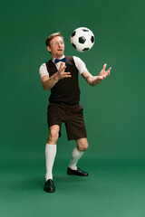 Naklejka na ściany i meble Portrait of man in stylish classical clothes, shorts and vest posing with football ball over green studio background. Concept of emotions, facial expression, lifestyle, retro fashion. Ad
