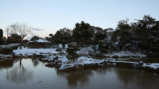 Partially frozen pond in snow covered Japanese garden at dawn