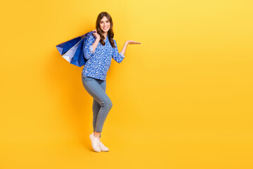 Full length portrait of cheerful person hold store bags hand hold demonstrate empty space isolated on yellow color background