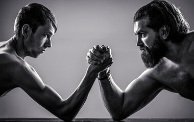 Arms wrestling thin hand, big strong arm in studio. Heavily muscled bearded man arm wrestling a...