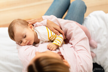Caring mother holding her adorable small sleeping baby girl on hands, singing lullaby, comforting...
