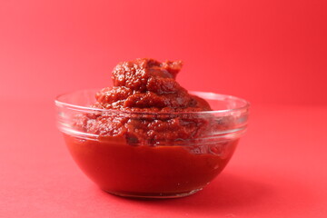 tomato paste in a glass sauce bowl on a red background monocolor. Food sauce red tomato food