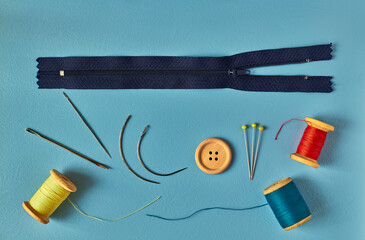 Sewing accessories - needles, thread, pins, and zipper on blue background