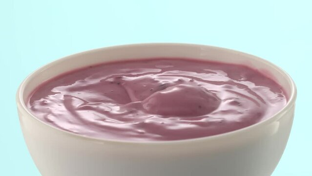 Spoon takes berry yogurt from a white bowl on a blue background. blueberry cream closeup. High quality 4k footage