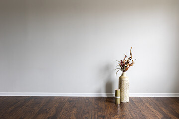 A hardwood floor houses an empty room with a dry plant arrangement in a clay vase placed next to a...