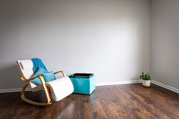 Domestic home interior as a background for video chat with potted plant in the room corner, rocking chair with teal colored blanked and pillows on hardwood floor.