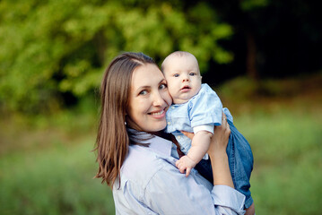 Loving mom carying of her newborn baby at park. Bright portrait of happy mum holding sleeping infant child on hands. Mother hugging her little 2 months old son.
