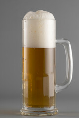 Light beer with foam in a tall glass on a gray background, light alcohol