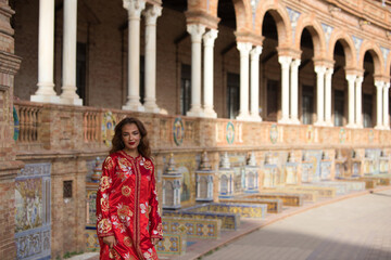 Fototapeta na wymiar A beautiful young woman wearing a traditional Moroccan red dress with gold and silver embroidery is on vacation in Seville, Spain.