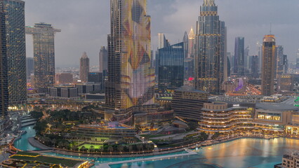 Naklejka na ściany i meble Skyscrapers rising above Dubai downtown day to night surrounded by modern buildings aerial top view