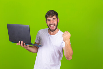 Image of happy excited young man posing isolated over green wall using laptop computer make winner...