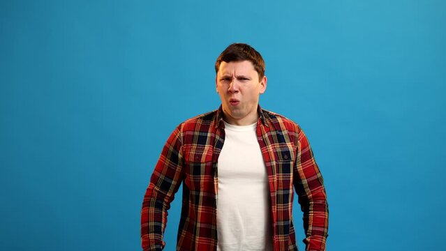 Young european man expressing disgust and aversion with frowning face and feeling gagging sensation, standing on blue studio background