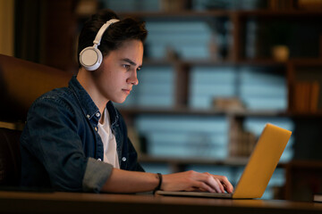 Concentrated young man working on laptop at dark office