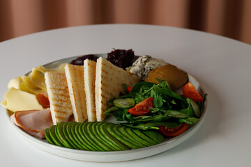 breakfast - tomatoes, cucumber, vegetable marrow, arugula, toasts, cheese, bacon and paste on white plate