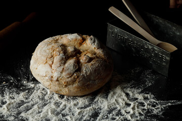 Traditional Freshly baked homemade loaf Bread, with flour and aluminum box near by on dark background. Artisan sourdough rye, wholegrain bread. Close up. Copy space